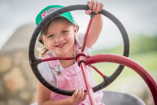 Young girl with hat holding tractor steering wheel